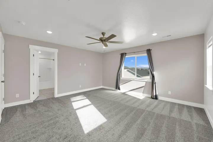 Spacious interior featuring neutral carpeting, a ceiling fan, recessed lighting, and a window with a sill