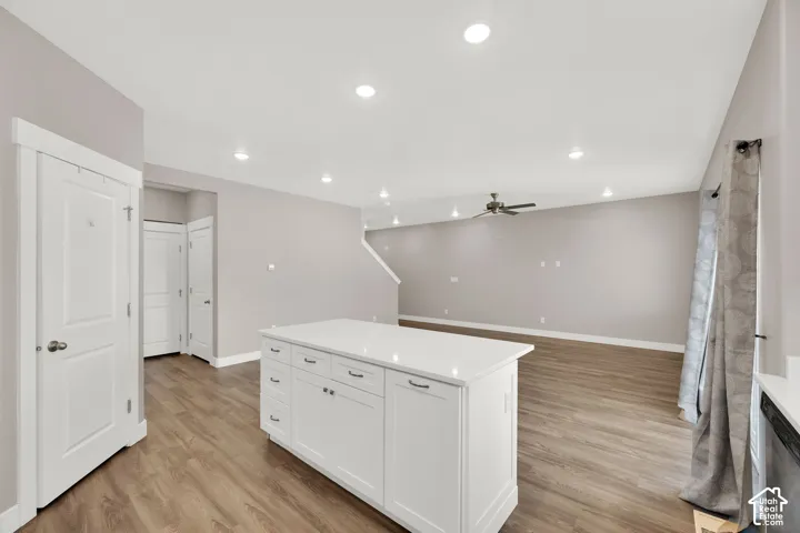 Open concept interior with wood-finish flooring, recessed lighting, and a kitchen island featuring white cabinetry and a light-toned countertop