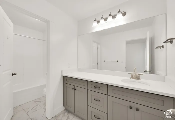 Single vanity with a white countertop and undermount sink, gray cabinetry, brushed nickel fixtures, and a four-light fixture