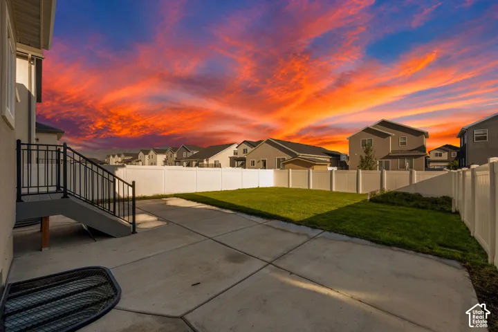 Concrete patio with a staircase featuring black railings, leading to a grassy yard enclosed by a white privacy fence