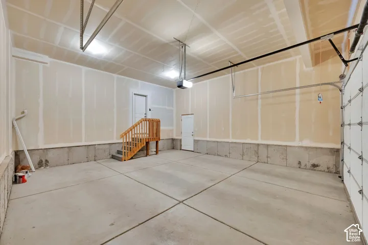 Spacious garage featuring a concrete floor, exposed drywall walls, and a wooden interior staircase