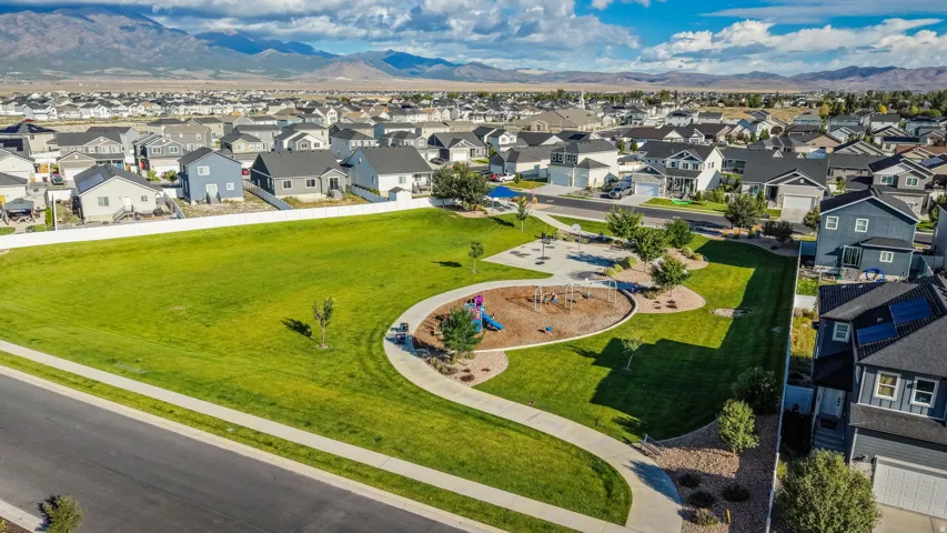 Expansive green space featuring a playground, paved walking paths, and mature landscaping within a residential community, with distant mountains