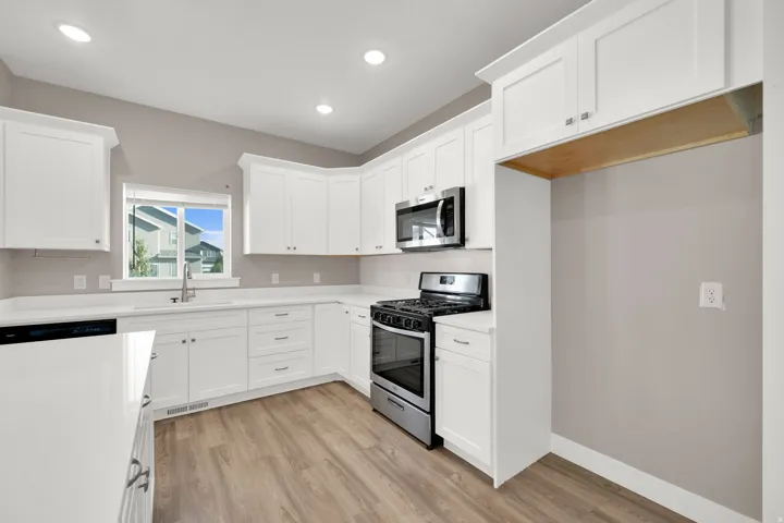 Modern kitchen featuring white cabinetry, light-toned wood-finish flooring, stainless steel appliances, white countertops, and recessed ceiling lighting