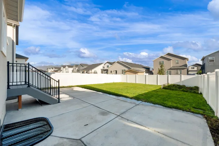 Expansive concrete patio with a finished deck and staircase featuring black metal railings, a manicured lawn area, and a white privacy fence