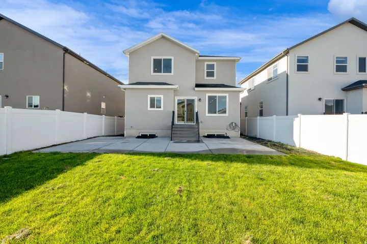 Rear exterior featuring a concrete patio, white privacy fencing, and a grassy yard