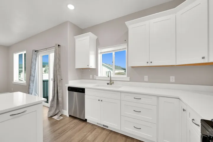 White shaker cabinetry with modern hardware, stainless steel dishwasher, wood-finish flooring, and white countertops