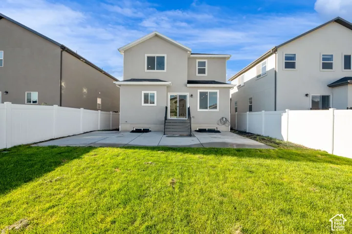 Rear exterior featuring a concrete patio, white privacy fencing, and a grassy yard