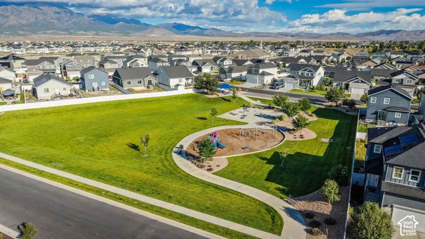 Expansive green space featuring a playground, paved walking paths, and mature landscaping within a residential community, with distant mountains