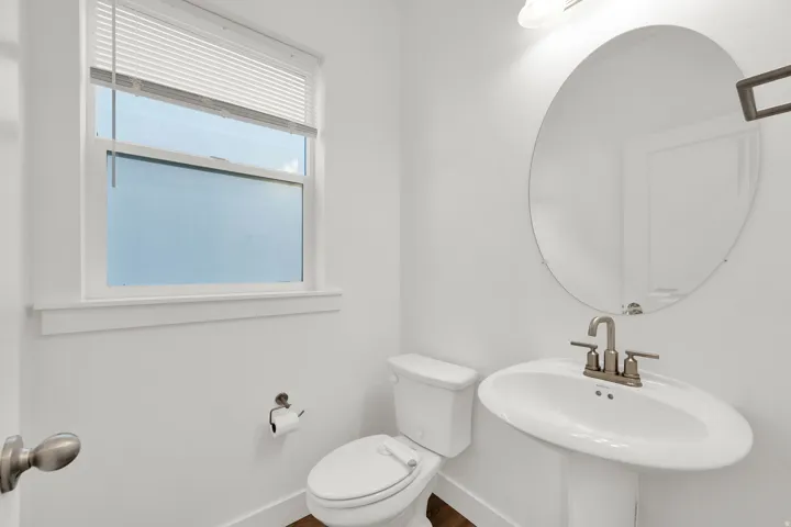 Pedestal sink with a brushed nickel faucet, an oval mirror, and a window with blinds