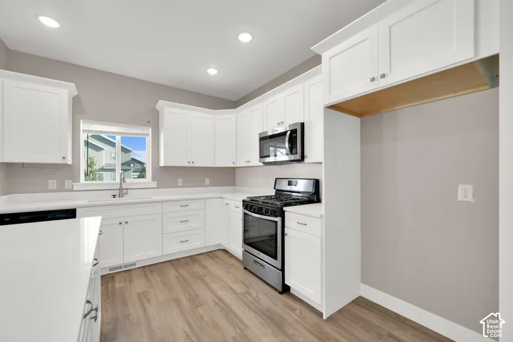Modern kitchen featuring white cabinetry, light-toned wood-finish flooring, stainless steel appliances, white countertops, and recessed ceiling lighting