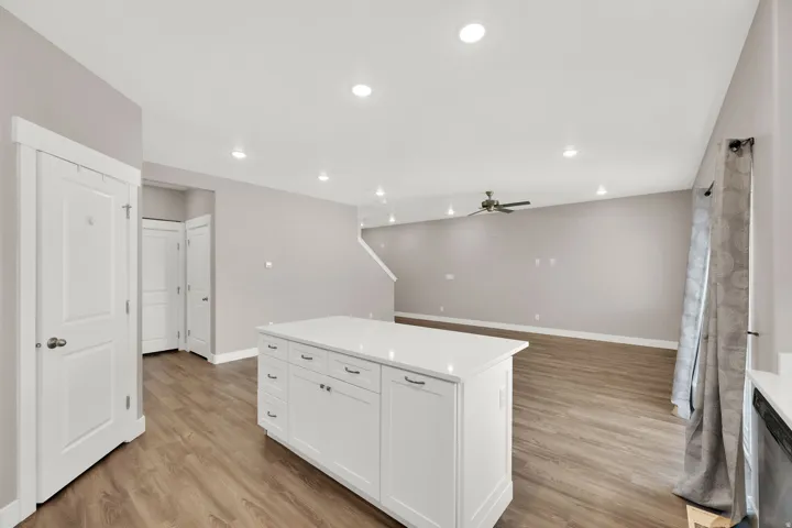 Open concept interior with wood-finish flooring, recessed lighting, and a kitchen island featuring white cabinetry and a light-toned countertop