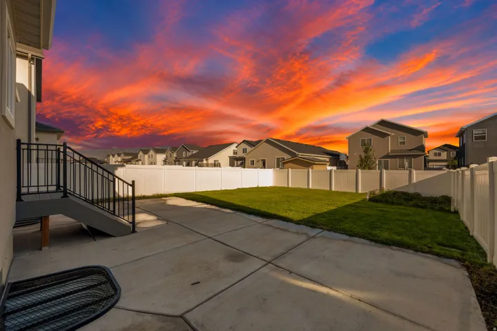 Concrete patio with a staircase featuring black railings, leading to a grassy yard enclosed by a white privacy fence