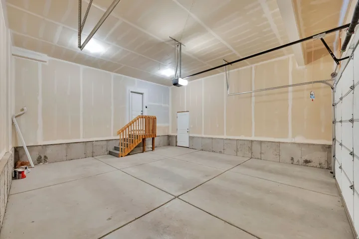 Spacious garage featuring a concrete floor, exposed drywall walls, and a wooden interior staircase