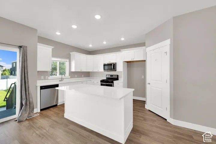 Kitchen featuring white cabinetry, stainless steel appliances, a center island with a solid surface countertop, wood-finish flooring, and recessed lighting