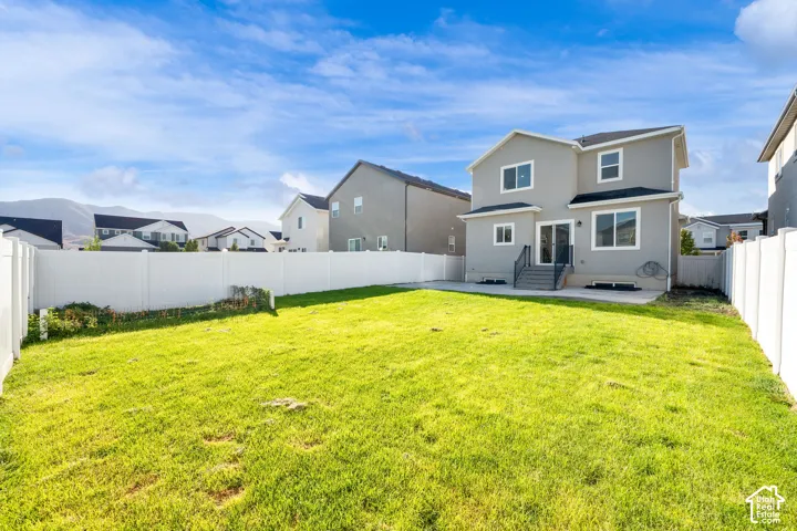 Expansive backyard featuring a manicured lawn, full vinyl privacy fencing, a concrete patio, and a two-story exterior with multiple windows