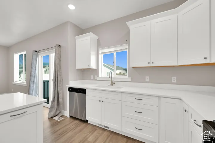 White shaker cabinetry with modern hardware, stainless steel dishwasher, wood-finish flooring, and white countertops