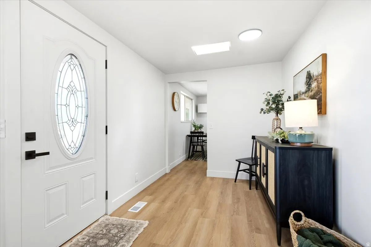 White entry door with decorative oval glass insert and matte black hardware, wood-finish flooring, recessed lighting, and a skylight