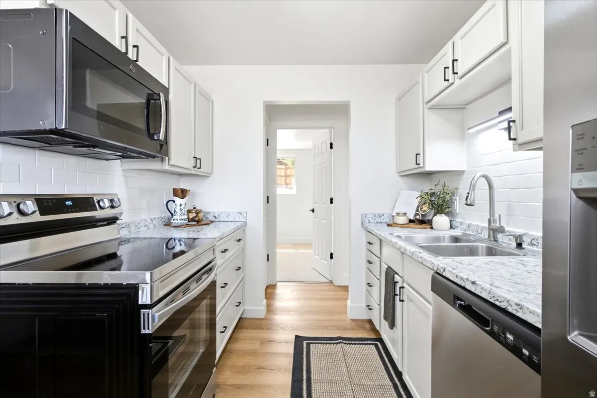 Galley kitchen featuring wood-finish flooring, white cabinetry with dark hardware, stainless steel appliances, and subway tile backsplash