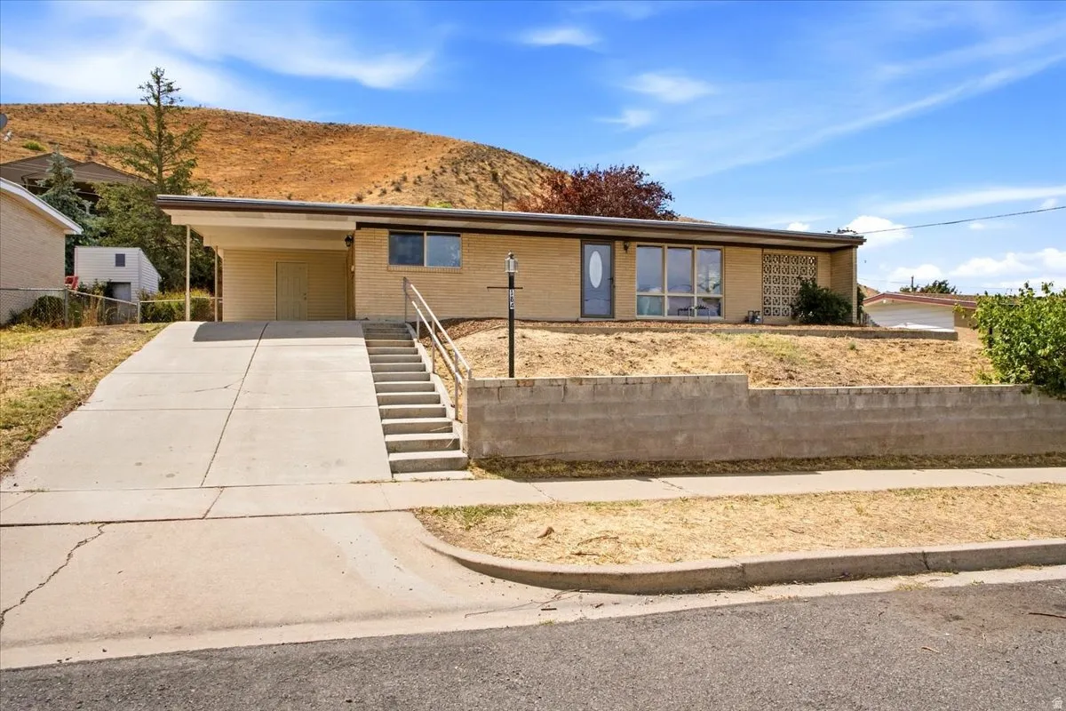 Brick exterior with a covered carport, concrete driveway, and concrete stairs with metal handrails