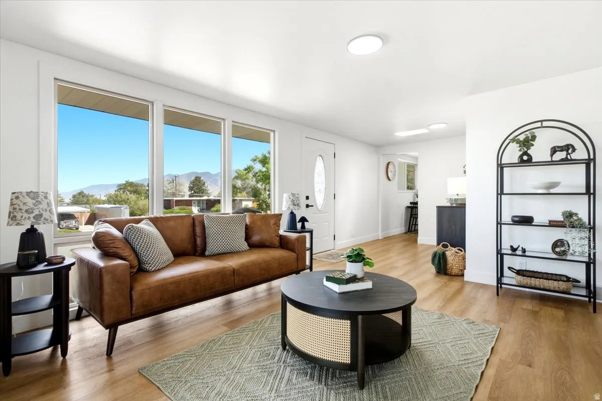 Bright living area with large windows, wood-finish flooring, recessed lighting, and a white entry door