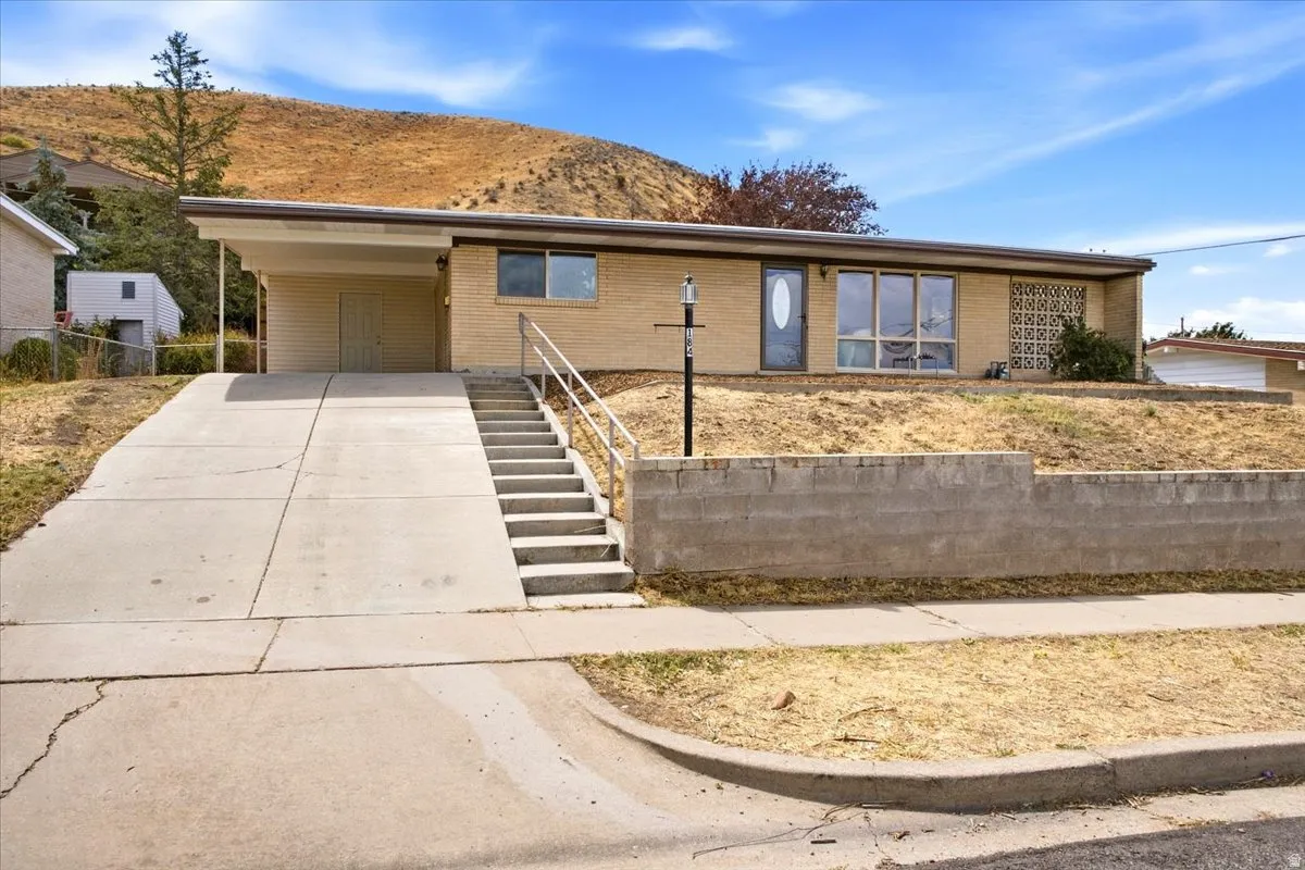 Brick exterior with a covered carport, concrete driveway, and front entry stairs featuring a metal railing