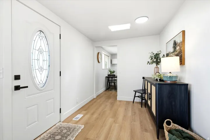 White entry door with decorative oval glass insert and matte black hardware, wood-finish flooring, recessed lighting, and a skylight
