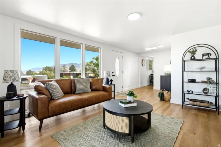 Bright living area with large windows, wood-finish flooring, recessed lighting, and a white entry door