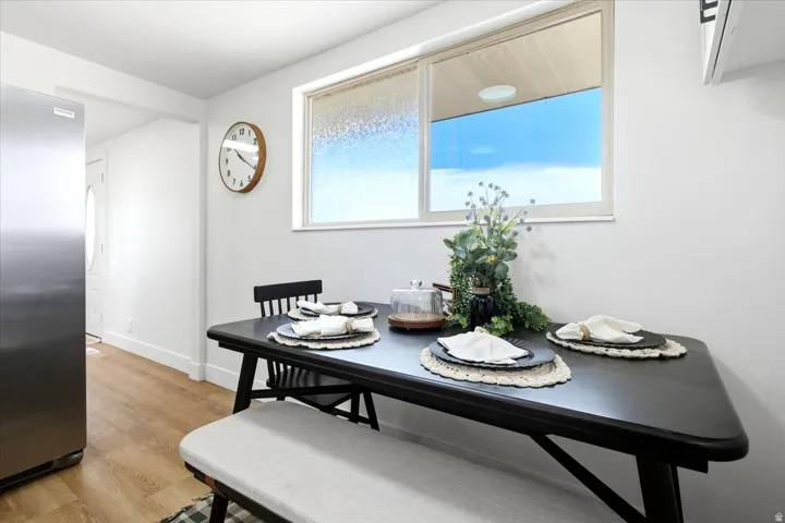 White walls, wood-finish flooring, stainless steel refrigerator, and a window with frosted lower pane