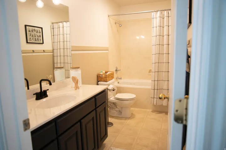 Bathroom featuring a dark wood vanity with a white countertop, a drop-in sink with a matte black faucet, a built-in bathtub with a shower, and light-toned tile flooring