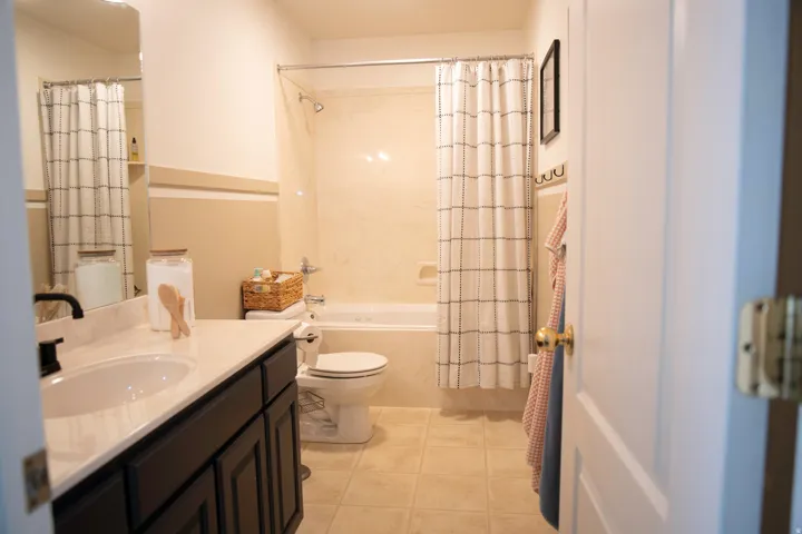 Galley-style bathroom featuring a dark wood vanity with dual sink, ceramic tile flooring, and an alcove shower with glass enclosure and coordinating tile surround