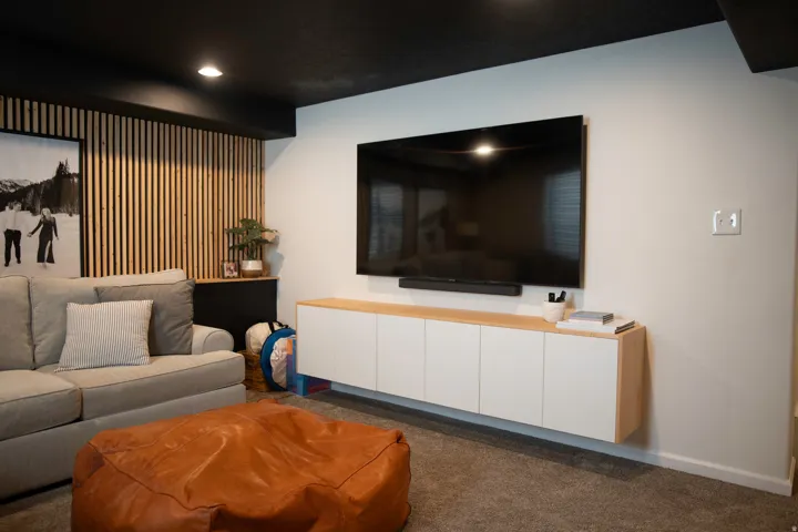 Wood slat accent wall, wall-mounted media console with white cabinetry, black ceiling, recessed lighting, and wall-mounted television