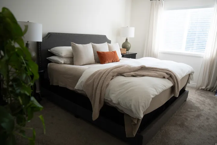 Primary suite with plush carpeting, large window with blinds, and neutral wall paint