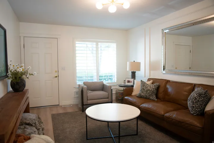 Recessed panel door, window with horizontal blinds, overhead ceiling fixture, decorative wall paneling, and wood-finish flooring