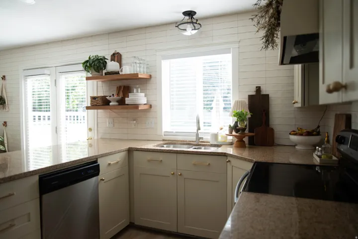 Light-toned cabinetry with gold-finish hardware, stainless steel dishwasher, brown speckled countertops, and a white tiled backsplash