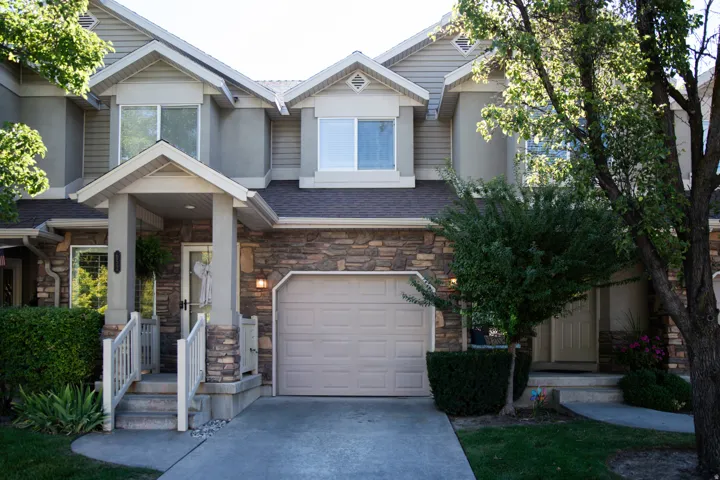 Stone and siding exterior with a covered porch entry, attached garage, and mature landscaping
