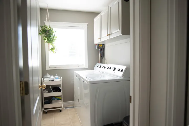 Laundry area featuring overhead cabinetry with gold-finish hardware, a window, and tile flooring