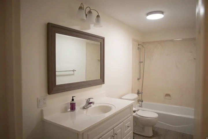 White vanity with integrated sink, chrome faucet, framed mirror, and overhead light fixture