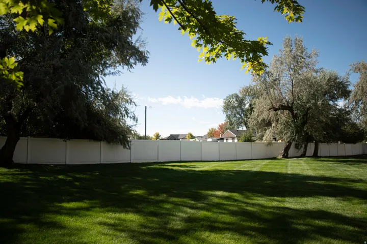 Expansive green lawn with mature trees and a privacy fence