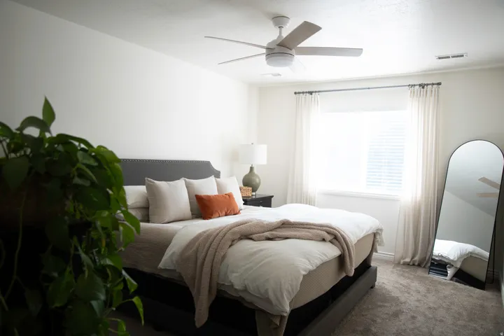 Primary suite with carpeted room featuring a ceiling fan, window with blinds, and white curtains