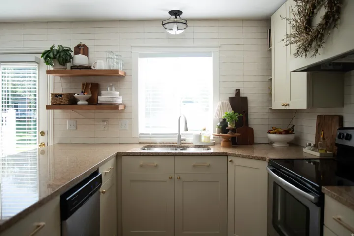 Kitchen featuring granite-look countertops, white subway tile backsplash, and light-toned cabinetry with brass hardware
