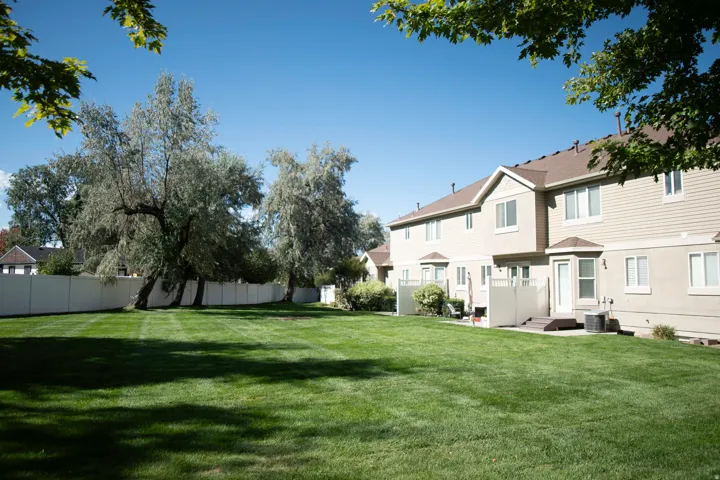 Expansive green lawn, mature trees, privacy fencing, multiple windows, and a patio area