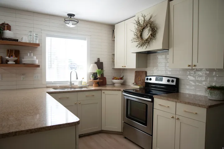 Light-toned cabinetry, speckled countertops, stainless steel range, and a white subway tile backsplash