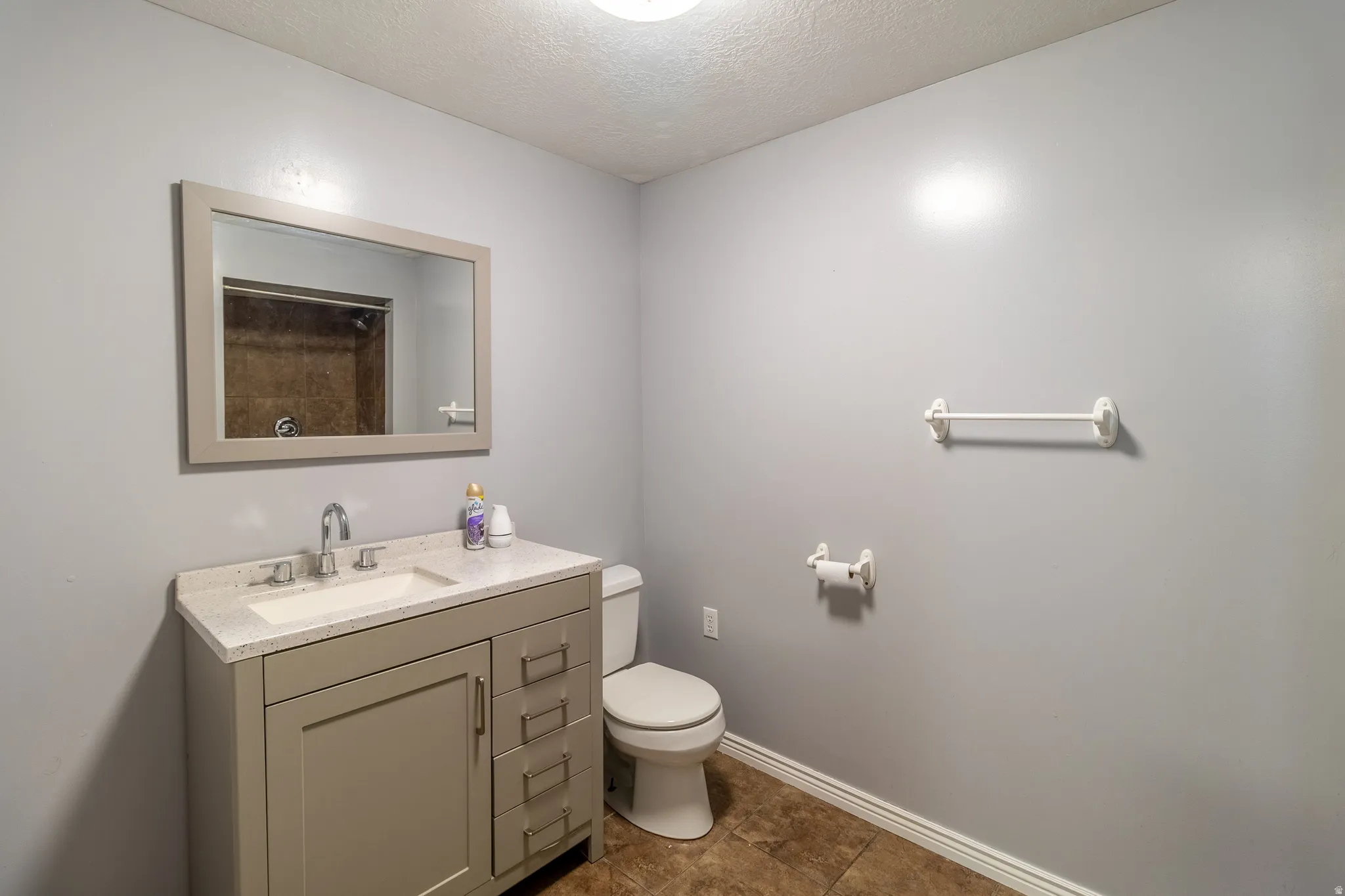 Vanity with integrated sink and chrome fixtures, framed wall mirror, tile flooring, and wall-mounted toilet paper holder