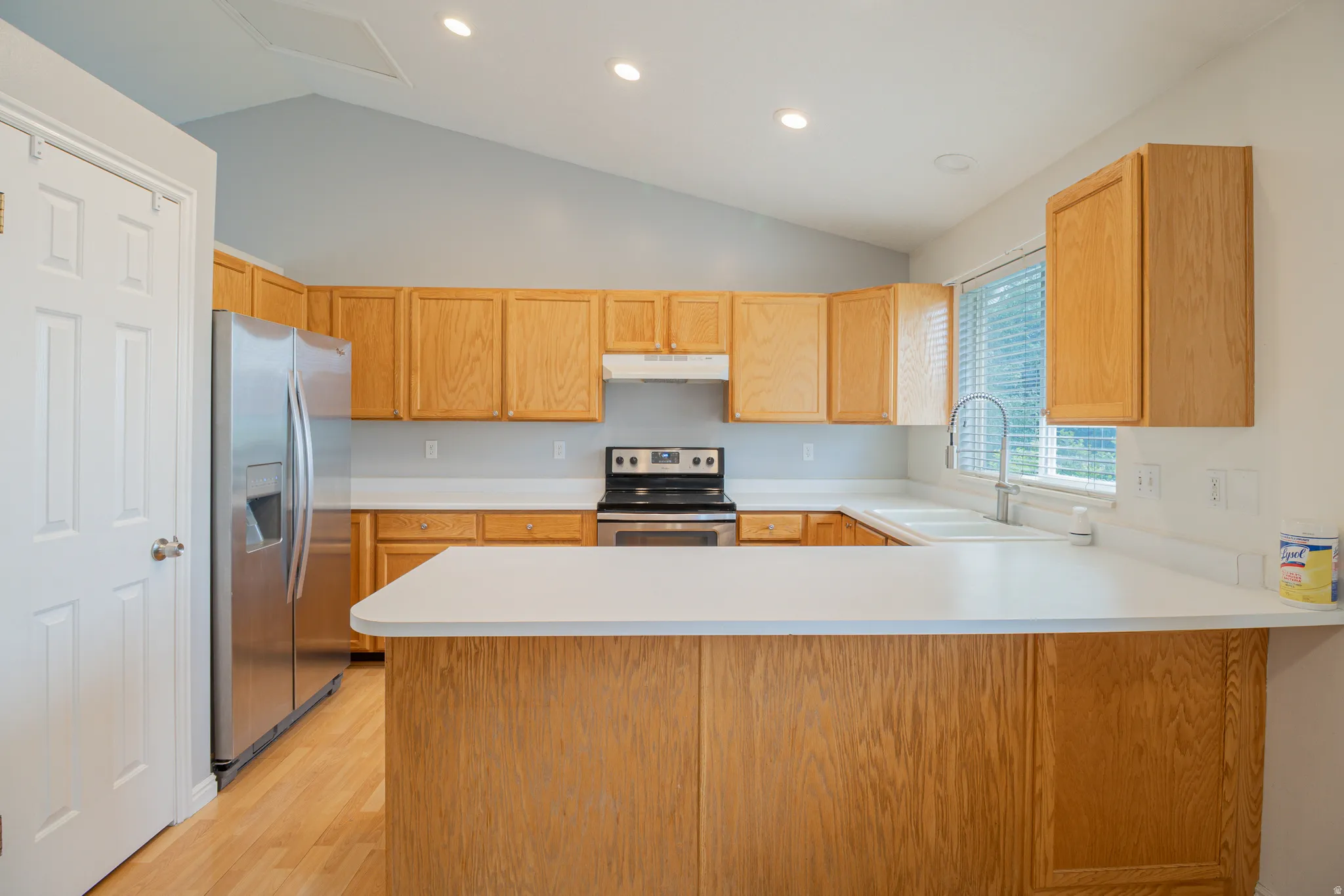 Kitchen featuring wood-finish cabinetry, stainless steel appliances, a double basin sink, and a high-arch faucet