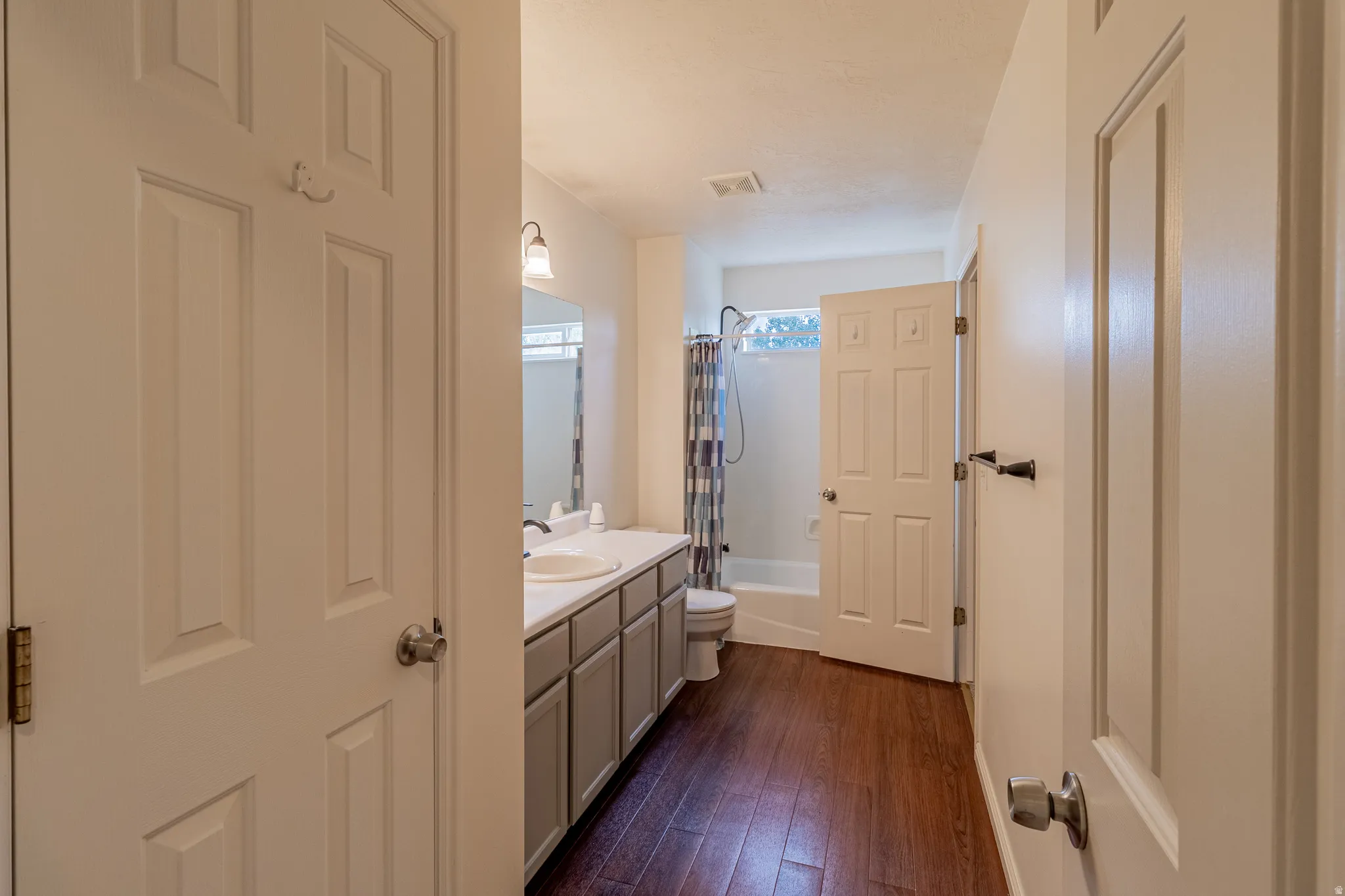 Elongated vanity with double sinks and ample storage, wood-finish flooring, and bright overhead lighting