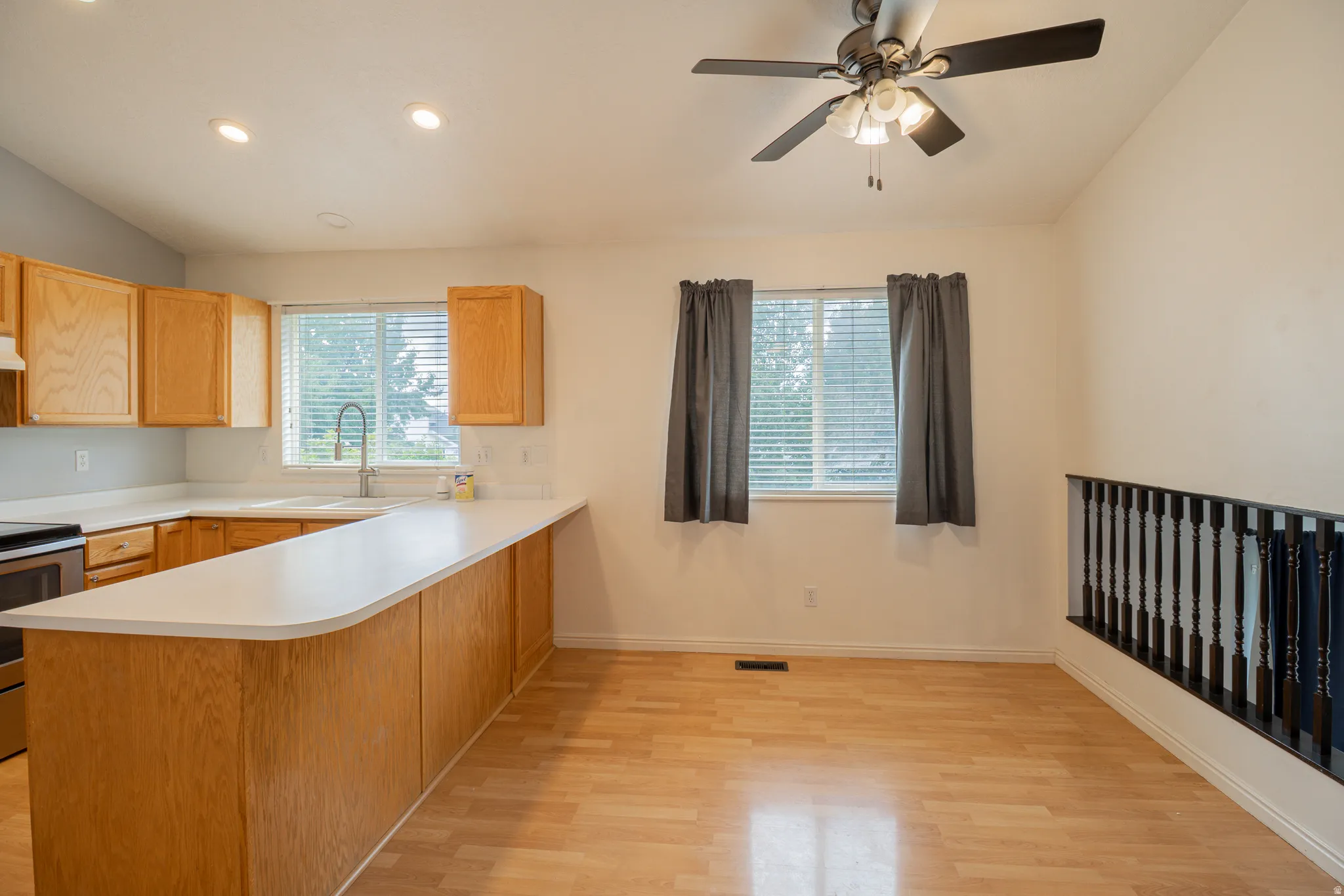Kitchen and dining area featuring wood-finish flooring, light wood cabinetry, a ceiling fan, and a breakfast bar with light countertops
