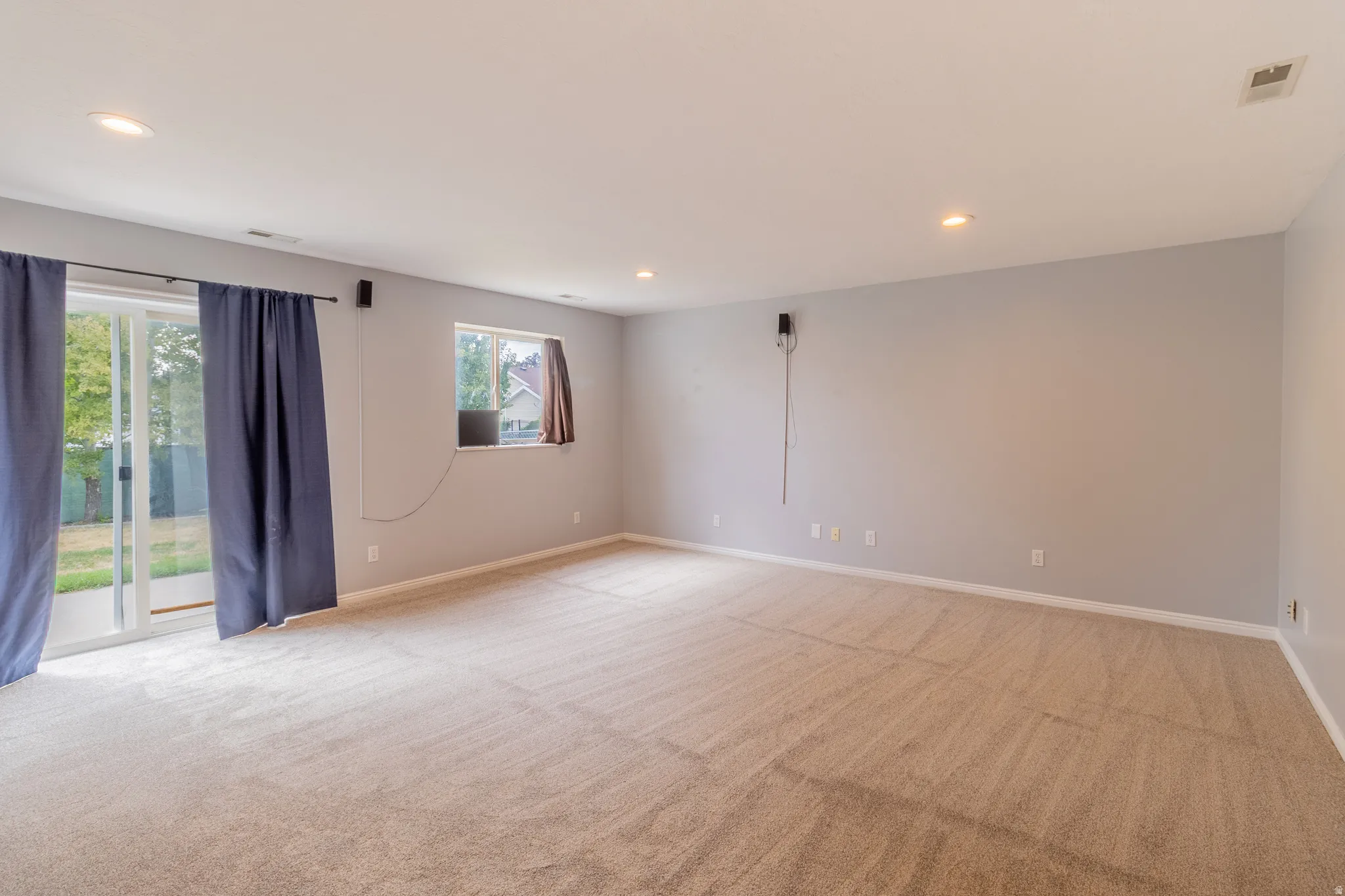 Spacious room featuring neutral carpeting, light gray walls, recessed lighting, and a glass sliding door to the exterior