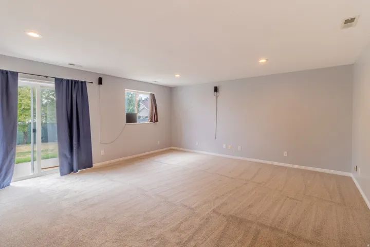 Spacious room featuring neutral carpeting, light gray walls, recessed lighting, and a glass sliding door to the exterior