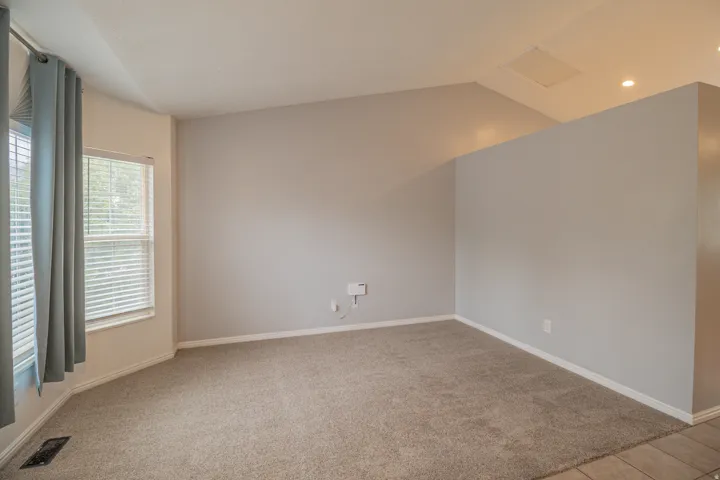 Carpeted living area with vaulted ceilings, recessed lighting, and ample natural light from multiple windows