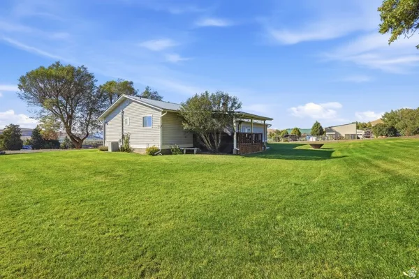 Expansive grassy area with a covered patio, mature trees, and light-colored siding